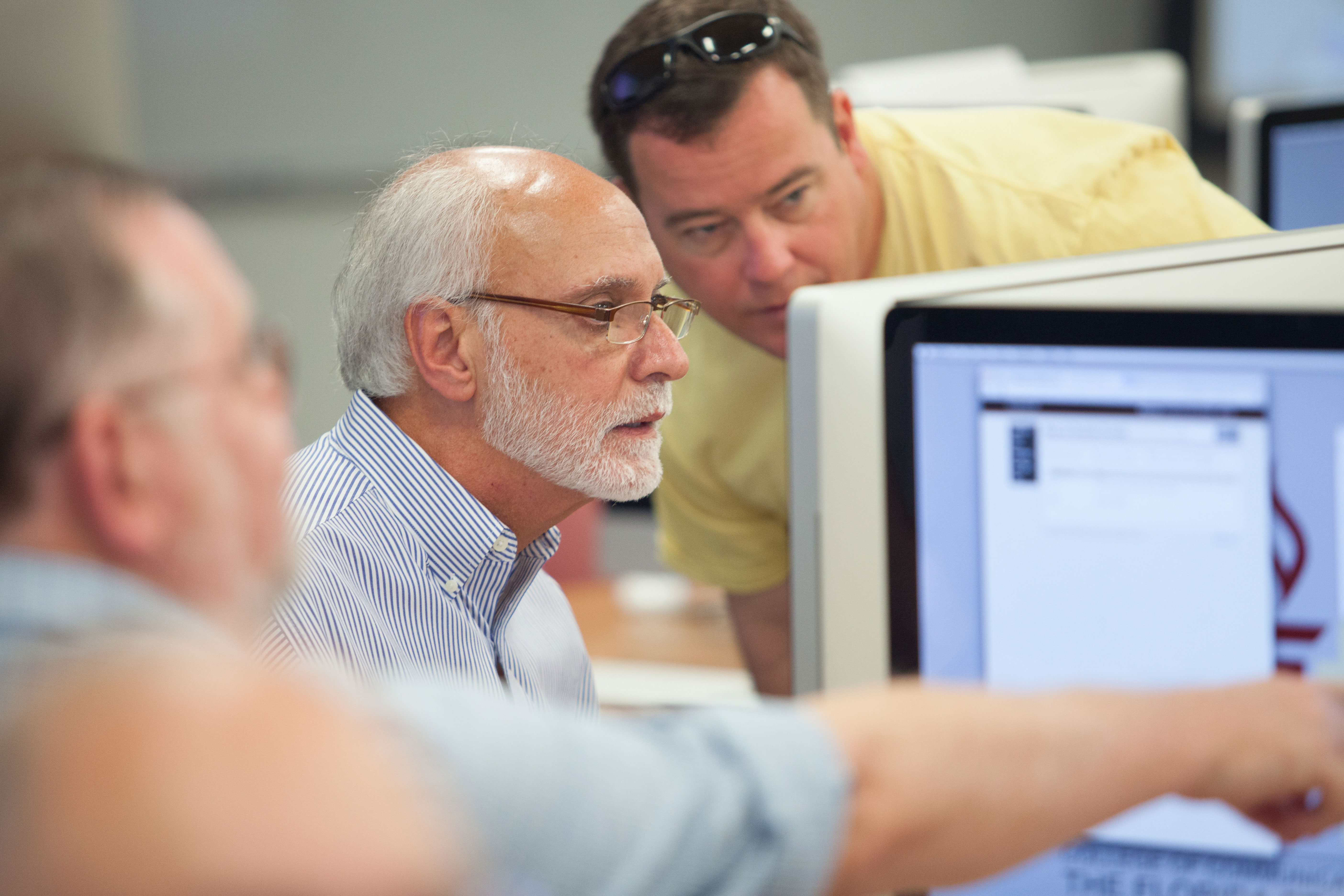 Male employee working on a desktop computer with two coworkers