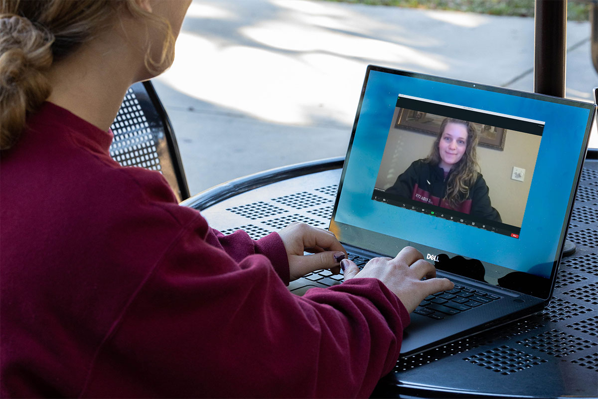 Female student sitting outside on her computer on Zoom. 